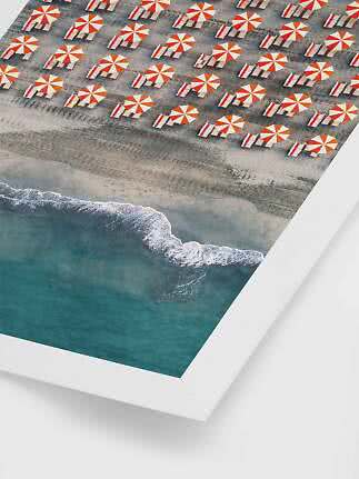 Luftfoto af strand med orange-hvide parasoller, liggestole og bølger ved kysten