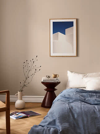 Bedroom with blue bedding, dark side table, vase, and framed artwork on a beige wall