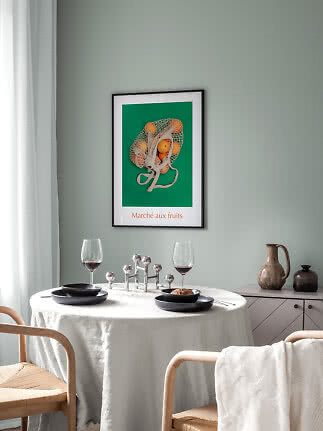 Angolo pranzo con tavolo rotondo, piatti neri, calici da vino e poster di frutta su parete verde.