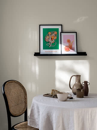 Angolo pranzo in stile natura morta con stoviglie, vasi in ceramica e due stampe di frutta incorniciate.