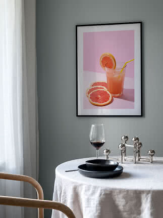 Inramad poster med grapefruktjuice och skivor mot rosa bakgrund ovanför ett dukat bord