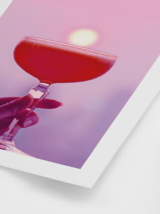 Hand hält ein Coupéglas mit rotem Cocktail vor rosa Hintergrund