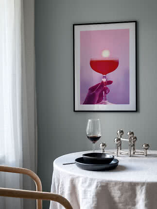 Gerahmter Print mit rosa Cocktailglas an grauer Wand über einem gedeckten Tisch