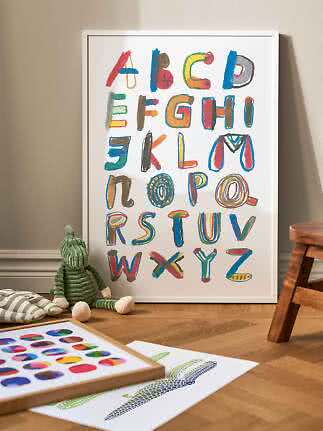 Framed alphabet poster with colorful hand-painted letters, leaning against the wall in a kids room