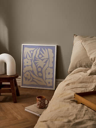 Soveværelse med beige sengetøj, skammel med hvid lampe og lilla blomsterplakat på gulvet
