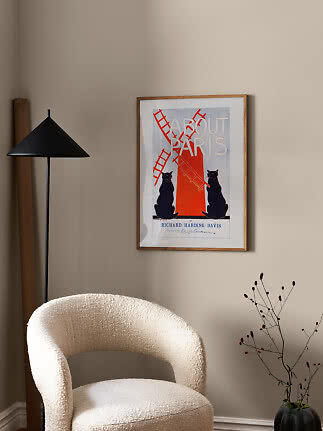 Indrammet About Paris-plakat på beige væg over hvid boucléstol ved sort gulvlampe