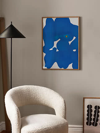 Abstract blue and white framed poster on a beige wall above a cream armchair.