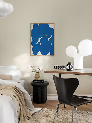Stylish bedroom with blue abstract wall art, black chair, table lamp, and small side table