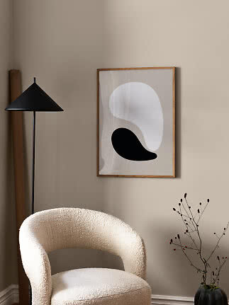 Lámina abstracta en blanco y negro con marco de madera sobre pared beige y sillón claro