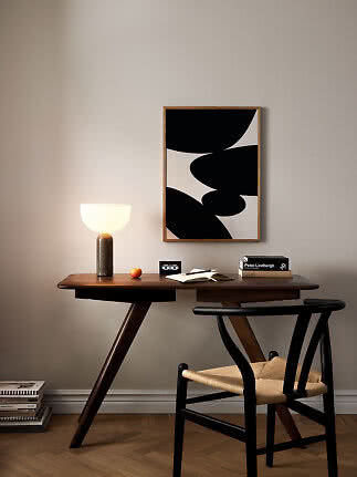 Schreibtisch aus dunklem Holz mit leuchtender Tischlampe, Stuhl und abstraktem Schwarz-Weiß-Bild