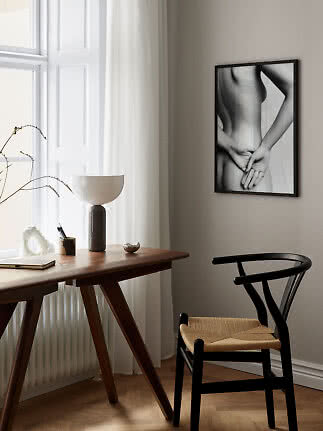 Minimalist workspace with wooden desk, black chair, table lamp, and black-and-white wall art.