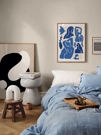 Cozy bedroom with light blue bedding, wooden tray, mug, and abstract framed wall art