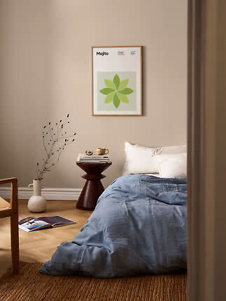 Schlafzimmer mit gerahmtem Mojito-Poster über einem Bett mit blauer Decke und kleinem Beistelltisch