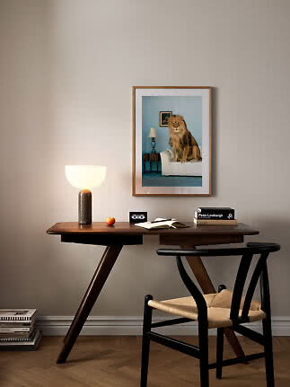 Skrivbord i trä med bordslampa, bok och stol under en inramad lejonbild på väggen