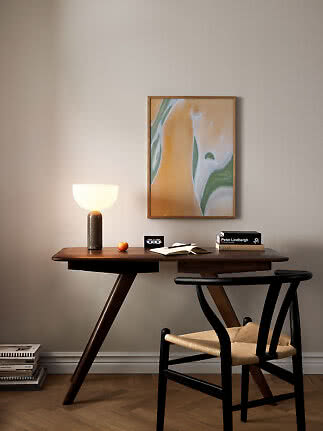 Dark wooden desk with lit table lamp, black chair and abstract painting on a beige wall
