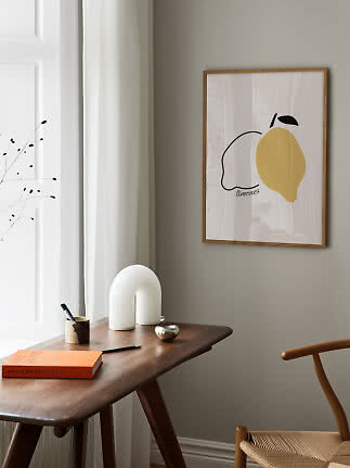 Inramad citronaffisch på grå vägg ovanför träbord i ett ljust, minimalistiskt rum