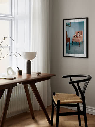 Svartinramad poster med pingviner i en rosa fåtölj ovanför ett träskrivbord vid fönstret.