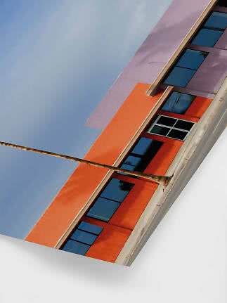 Schräg aufgenommenes modernes Gebäude mit orange-lila Fassade, dunklen Fenstern und Palme
