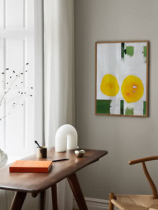 Abstract framed wall art above a wooden desk in a bright, modern room corner