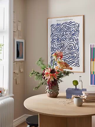 Bright dining nook with round wooden table, floral vase, and framed art prints on the wall
