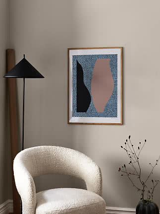Lámina abstracta enmarcada en pared beige sobre sillón blanco junto a lámpara de pie negra