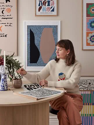 Mujer en mesa con pinceles y láminas artísticas en un estudio creativo