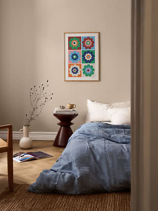 Sovrum med blått täcke, litet sidobord och färgglad blomposter på väggen