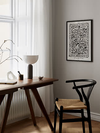Black framed abstract poster above desk with chair by window and white curtains