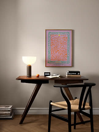 Dark wooden desk with glowing table lamp, black chair and pink framed poster on the wall