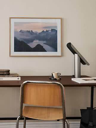 Home office with wooden chair, desk lamp, and framed mountain landscape print on the wall