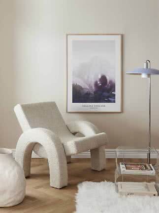 Poster of a misty mountain landscape in a light wood frame above a cream lounge chair.