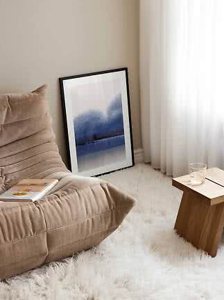 Cozy corner with beige lounge chair, blue abstract art print, small wooden table and white rug
