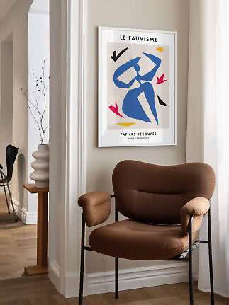 Framed Fauvism poster with blue abstract figure above a brown armchair by the window
