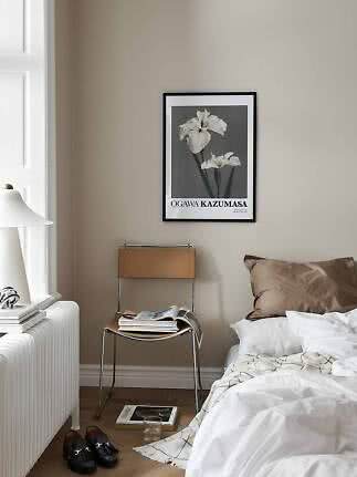 Soveværelse med indrammet blomsterplakat over stol, seng med hvidt sengetøj og lampe ved vindue