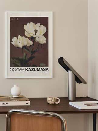 Indrammet blomsterplakat med hvide pæoner over et skrivebord med lampe, bøger og kop