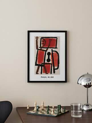 Oprawiony plakat Paul Klee z abstrakcyjną czerwono-czarną figurą nad stołem z szachownicą