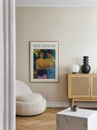 Framed Paul Gauguin poster on a beige wall above a boucle chair and wooden cabinet