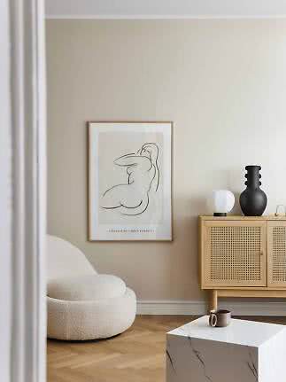 Minimalist living room with cream lounge chair, framed line art and light wood cabinet with black vase.