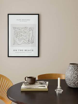 Framed art poster with sketch of nude figures in a beach scene above a dark table