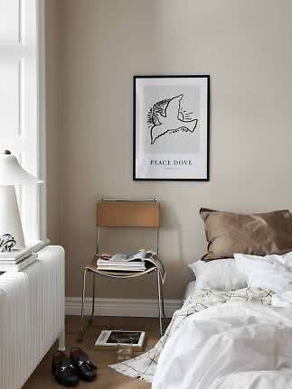 Schlafzimmer mit Peace-Dove-Poster über Stuhl, weißem Bett, Lampe und Schuhen auf Holzboden