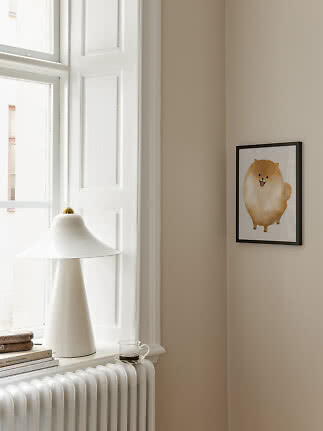 Poster incorniciato con tenero cane soffice su parete beige accanto a finestra e lampada bianca