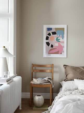 Rincón de dormitorio con póster abstracto, silla de madera, cama, lámpara blanca y jarrón en el suelo