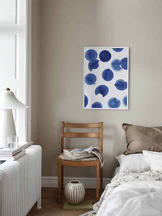 Framed print with blue abstract circles above a chair beside a bed