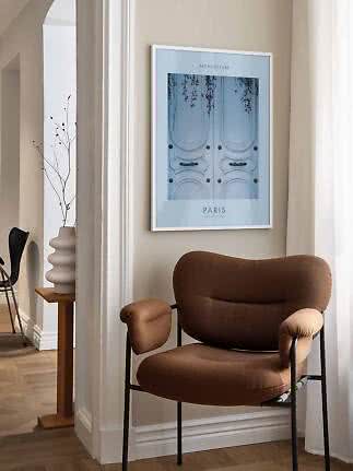 Gerahmtes Paris-Poster mit hellblauer Tür hängt über einem braunen Sessel in hellem Raum