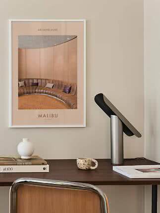 Poster di architettura incorniciato sopra una scrivania con lampada, vaso, tazza e libri