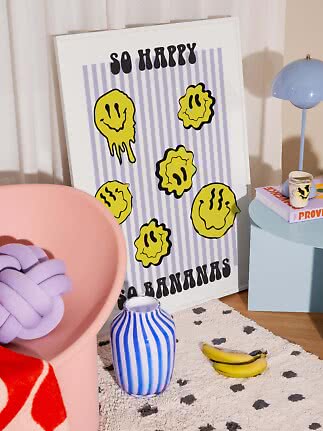 Poster colorato con faccine gialle e scritta “So Happy So Bananas” in una stanza moderna