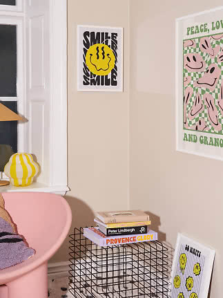 Farverigt hjørne med smile-plakat, pink stol, gulstribet lampe og bøger på sort trådbord