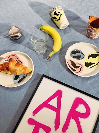 Frukostscen med croissant, banan, glas, mugg och konstnärliga tallrikar på blå duk