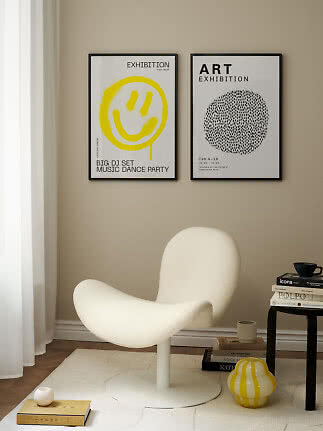 To indrammede kunstplakater over en hvid loungestol i et moderne beige hjørne.