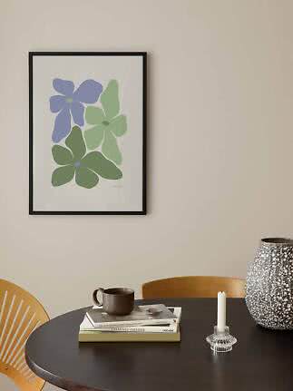 Affiche florale encadrée avec fleurs abstraites bleues et vertes sur mur clair au-dessus d'une table noire